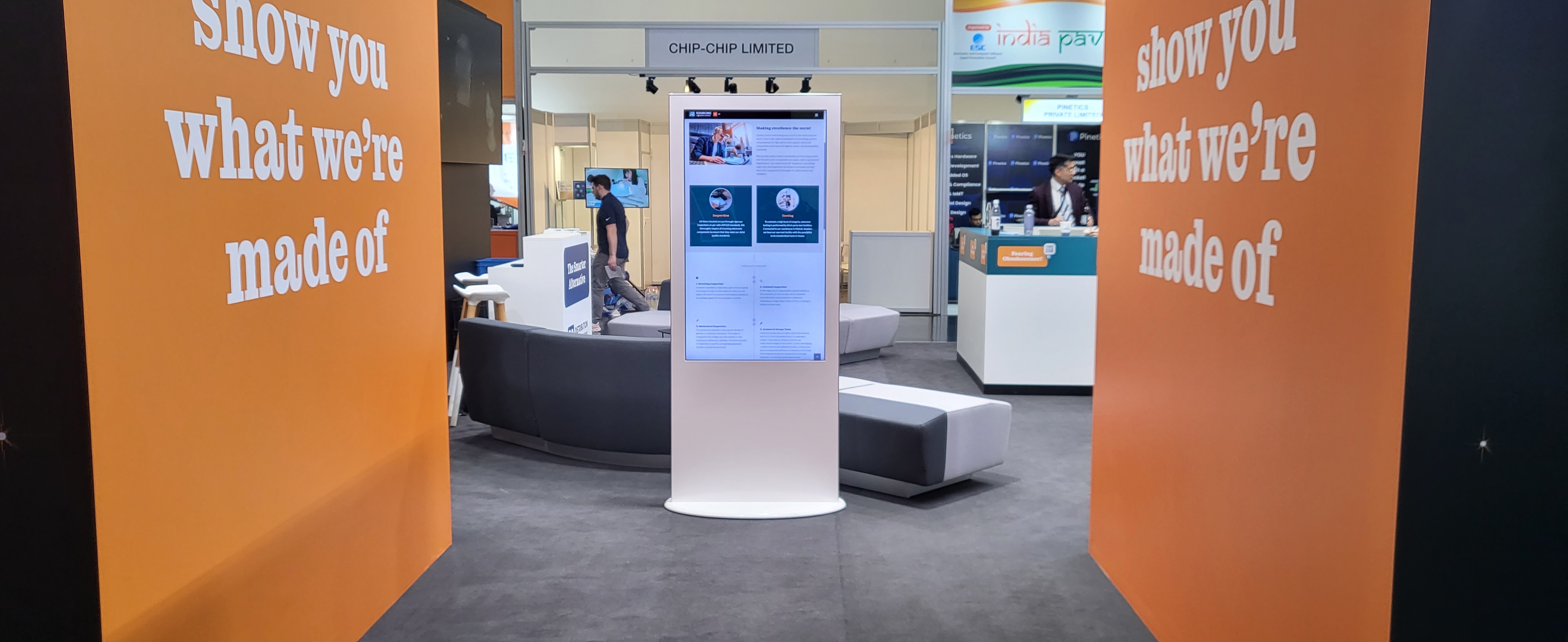 Weiße Touchscreen-Stele im Einsatz auf einem Messestand mit orangen Bannern